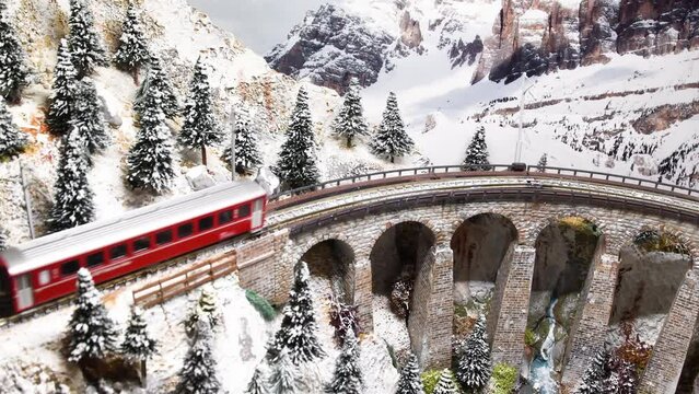 red model train in miniature passing on viaduct. Model railway, alps moutain ambientation.