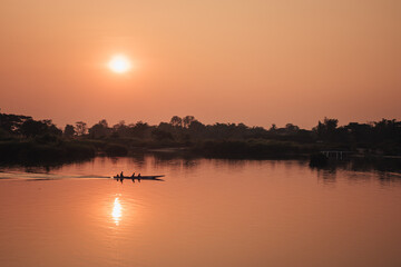Don Det, Laos - January 19th, 2020 : fiery orange sunset on the Mekong river in Don Det, southern Laos with a boat on the water.