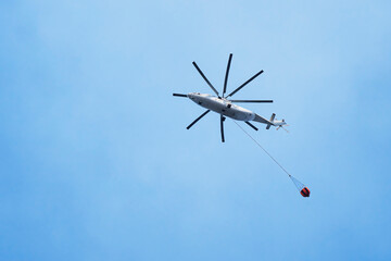 Helicopter going to fire area to extinguish forest fire. Helicopter with a water bucket on a blue sky.