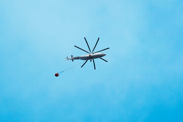 Aerial firefighting with helicopter. Helicopter carries water against the background of the blue sky.