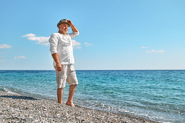 Happy middle-aged bearded man walking along beach. Concept of leisure activities, wellness, freedom, tourism, lifestyle and nature. Tourism in summertime.