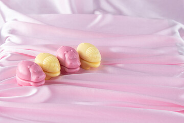 Various edible animals made from chewing marmalade with the addition of natural juices.  Yellow and pink flowers among the most delicate folds of an elegant pink fabric.  Children's sweets