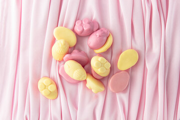 Various edible animals made from chewing marmalade with the addition of natural juices.  Yellow and pink flowers among the most delicate folds of an elegant pink fabric.  Children's sweets