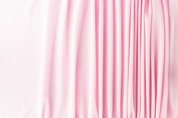 Many narrow vertical folds on a delicate pink fabric turn into a smooth background.