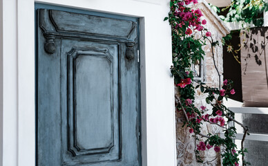 tiny wooden door at mediterranean or aegean typical house facade, blooming bougainvillaea or paperflower, inner yard