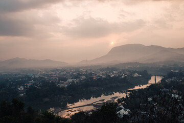 Luang Prabang, Laos - January 29th, 2020 : view from Mount Phousi on the city of Luang Prabang, the Mekong river and the surrounding mountains in the background at sunrise.