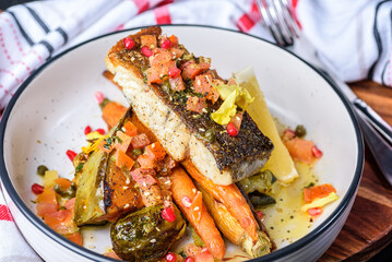 A serving of crispy skin grilled barramundi fish with roast vegetables in a round white bowl