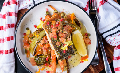 A serving of crispy skin grilled barramundi fish with roast vegetables in a round white bowl