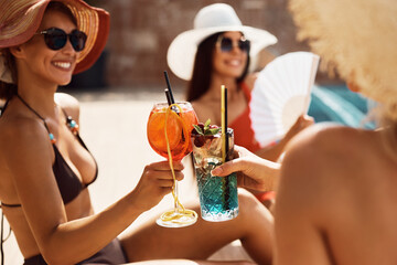 Close up of women toast with cocktails during summer day by swimming pool.
