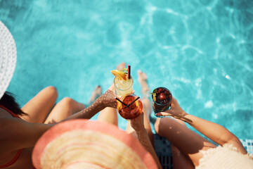Close up of women toasting with summer cocktails at swimming pool.