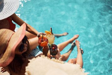 Close up of women toasting with cocktails while relaxing on summer day at the pool.
