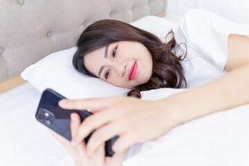Obraz na płótnie Canvas Young Asian woman using smartphone on bed