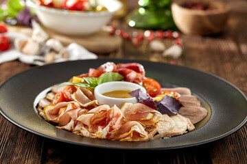 Meat platter on black plate on wooden background. Meat assorted with sauce and basil. Composition with Italian antipasti in rustic style. Meat delicatessen on dark wooden table with ingredients.