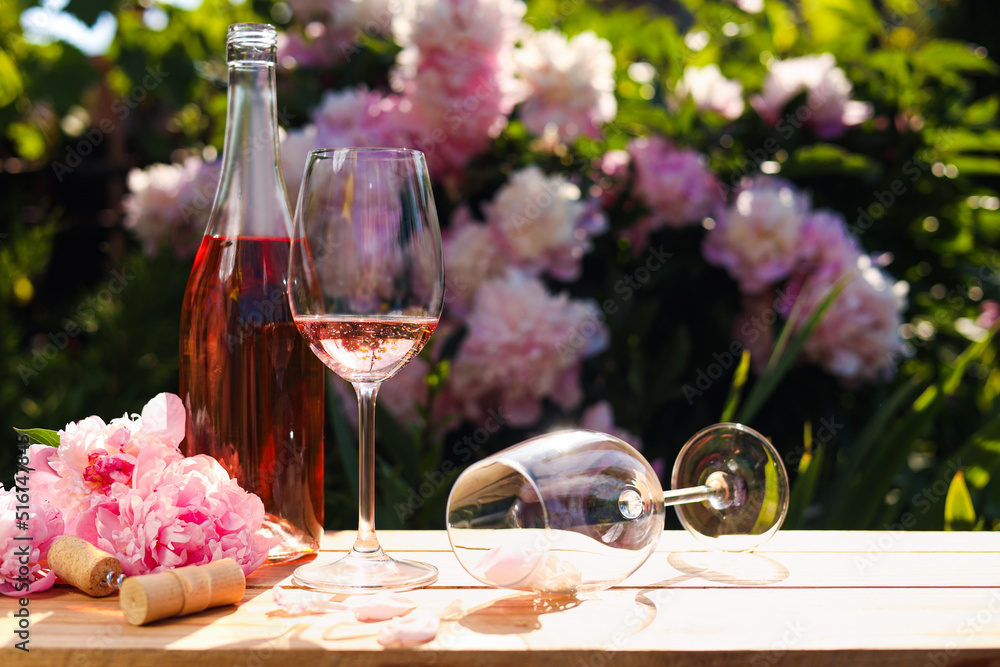 Canvas Prints Bottle and glass of rose wine near beautiful peonies on wooden table in garden. Space for text