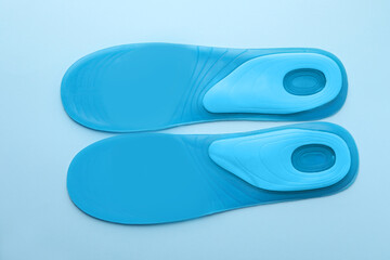 Turquoise orthopedic insoles on light blue background, flat lay
