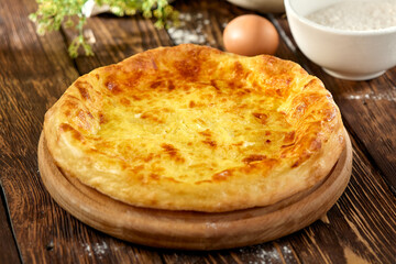 Traditional georgian pastry - megrelian khachapuri with cheese. Georgian cheese pie on wooden background in rustic style. Megrelian khachapuri with ingredients. Georgian cuisine.