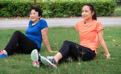 Asia senior woman and teenager rest sit on grass after walking or jogging exercise at park	