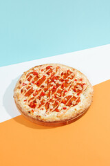 Italian pizza with pepperoni and spicy sauce on coloured background.Spicy pizza with salami, tomato and paprika in minimal style on blue color. American pizza delivery concept with color backdrop.