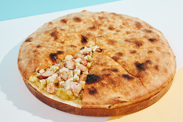 Italian closed pizza with cheese, potatoes and chicken on coloured background. Chicken pie with cheese and potatoes in minimal style. American pizza delivery concept with color backdrop.