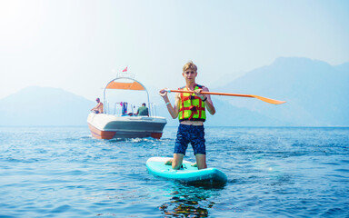 Inflatable stand-up paddle board. Teen in life jacket costs on a sap board looking at the camera.