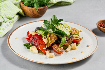 Salad with grilled vegetables, greens and cheese on concrete background. Warm salad with paprika, zucchini, eggplant and tomato on grill. Aesthetic composition with veggie salad. Summer menu concept.