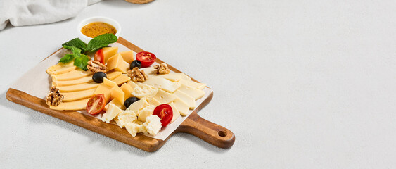 Cheese platter with nuts, honey sauce and olives on wood board. Cheeseboard on white concrete...
