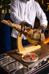 Girl cuts jamon, selective focus. The man cuts the meat. Prosciutto, ham cutter with a knife...