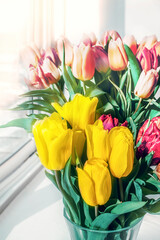 Multicolored tulips stand on the window in a glass vase
