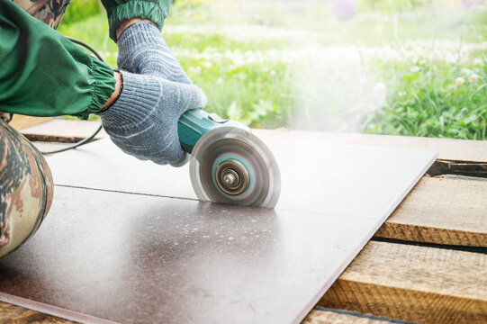 hands of a locksmith in special clothes works in the production of home repairs. Processing of ceramics with an angle grinder. Cuts ceramic tiles with an electric saw