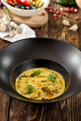 Traditional georgian dish - sacivi with chicken and walnut sauce. Roasted chicken in walnut sauce on black plate. Georgian food on wooden background. Meat appetizer in rustic style on wood table.