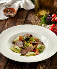 Steak salad with zucchini, tomatoes and lettuce on white plate. Fresh salad with roast beef and vegetables on wooden table in rustic style. Meat and vegetables salad on dark wooden background.