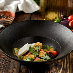 Salad with crispy eggplant, feta cheese and tomatoes on black plate. Fresh salad with eggplant and vegetables on wooden table in rustic style. aubergine and feta salad on dark wooden background.
