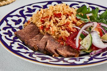 Traditional uzbek food - plov with beef. Eastern cuisine - pilaf with rice, meat and spices. Plov with beef on traditional uzbek plate. Composition of oriental ceramic plate with pilaf. - obrazy, fototapety, plakaty