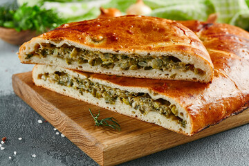 Traditional russian cabbage pie on wooden board with ingredients. Composition with cabbage pie on concrete background with textile and spices. Homemade pie with cabbage in rustic style on gray table.