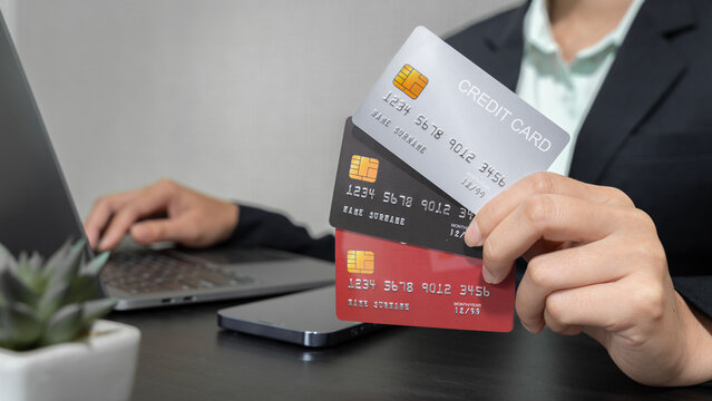 Businessman showing his own three credit cards Available in red, gray and black. On a desk with a laptop and phone placed in the office.