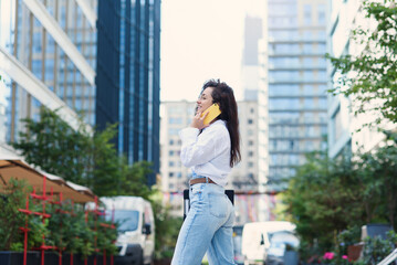 Young business woman walking across the road with tablet among the skyscrapers and speaks on the phone.