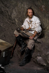 Sea robber captain of pirate ship armed with treasure chest in cave. Concept historical halloween. Filibuster cosplay