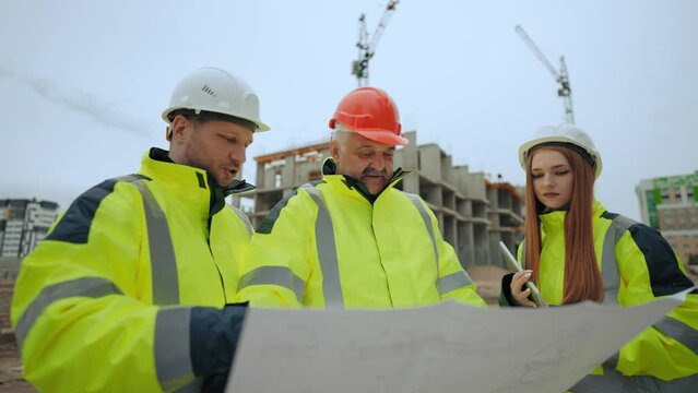building inspection in modern construction area, two men and woman are viewing plan and discussing