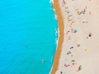 holiday background. Beach coastline with tourists sunbathing and swimming in turquoise sea. View from above with copy space for your text