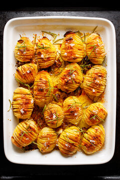 Traditional Swedish dish Hasselback potatoes with additional herbs and spices  in a ceramic baking dish, top view