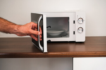 a man puts a plate in the microwave to warm up his food