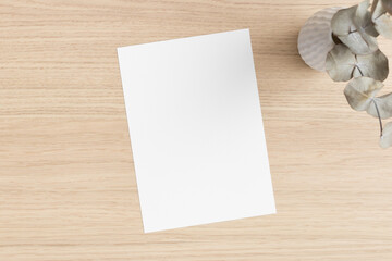 White invitation card mockup with an eucalyptus on the wooden table. 5x7 ratio, similar to A6, A5.