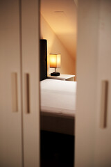a white wardrobe with a mirror reflecting a table lamp of warm light. beautiful bedroom interior in scandinavian style