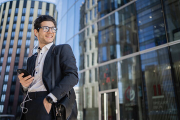 Fototapeta premium A man with glasses writes a text message to a client on the phone, goes to work in the office in a business suit