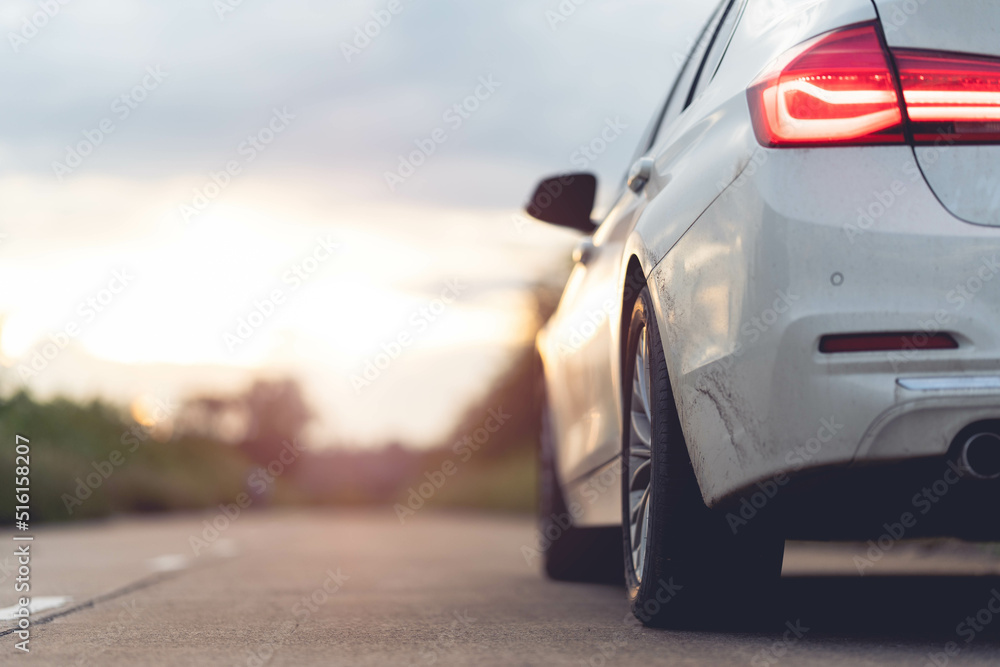 Wall mural behind a beautiful white car parked on a road with beautiful sunsets. with space for text.