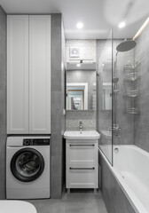 Small modern bathroom in gray tones with washing machine, white vanity, mirrored frame and fittings. High quality photo