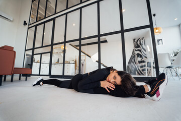 Young female wearing black sports suit exercising yoga pose indoors.