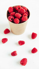 Fresh red raspberries in a paper cup on a white table background