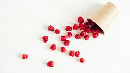 Fresh red raspberries in a paper cup on a white table background