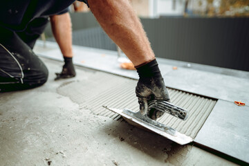Flooring and tiling. Hand of professional construction worker placing floor tiles on adhesive surface on balcony - 516161008